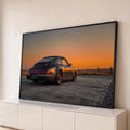 Porsche 911 cinza visto de trás sob céu laranja do pôr do sol em campo seco, quadro decorativo