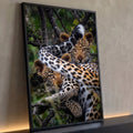 Dois filhotes de leopardo deitados em galho de árvore com folhas verdes ao fundo, quadro decorativo
