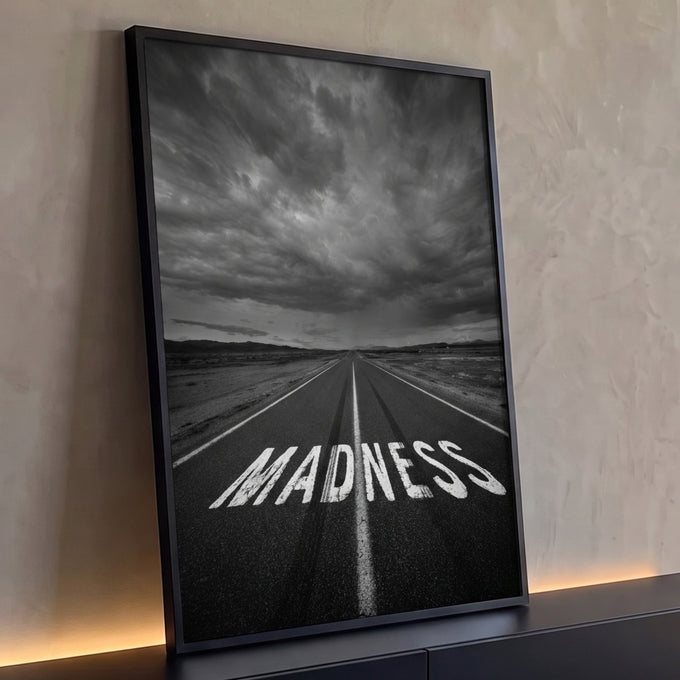 Estrada com a palavra MADNESS pintada no asfalto sob céu tempestuoso em preto e branco, quadro decorativo