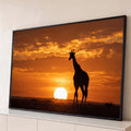 Silhueta de girafa diante do sol se pondo na savana africana sob céu laranja, quadro decorativo