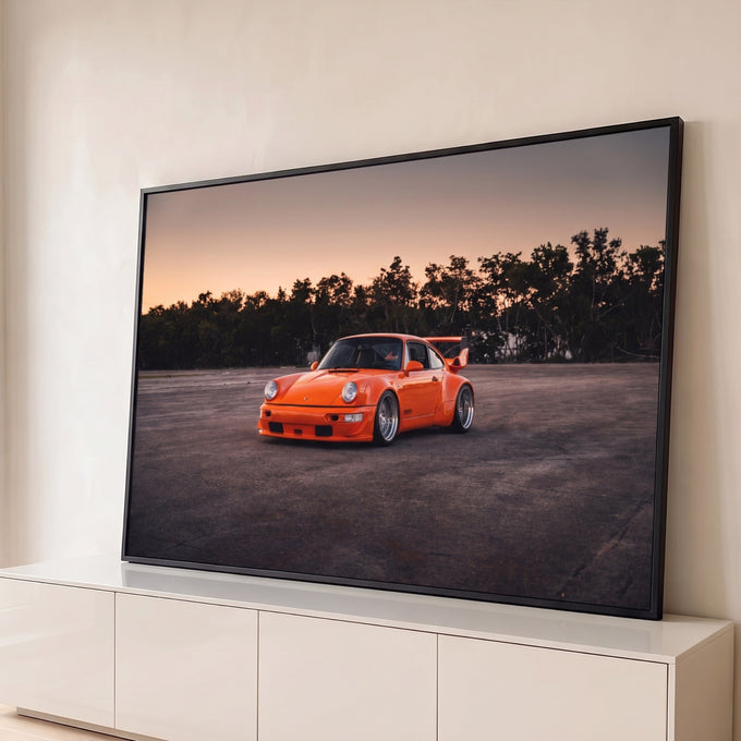 Porsche 911 RWB laranja com aerofólio em pátio de asfalto ao entardecer, árvores ao fundo, quadro decorativo