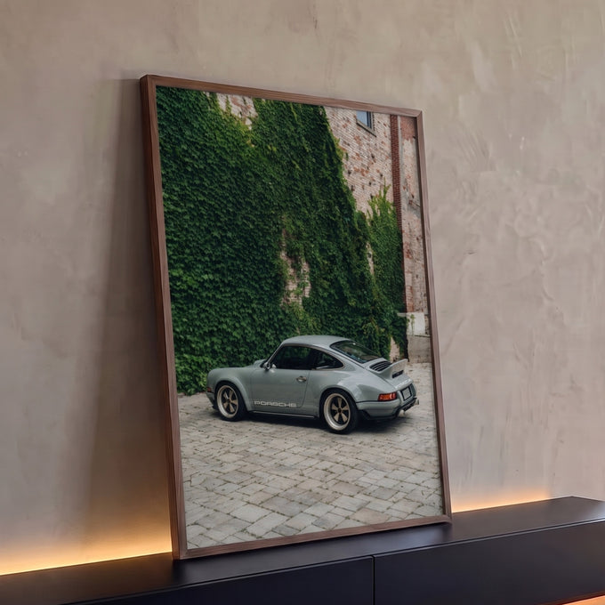 Porsche 911 cinza estacionado em pátio de pedra diante de muro de tijolos coberto de hera, quadro decorativo