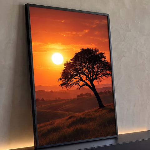 Árvore inclinada em silhueta sobre colinas com sol baixo e céu laranja no pôr do sol, quadro decorativo