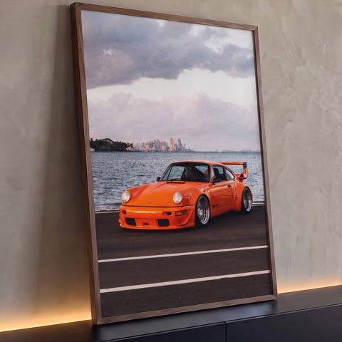Quadro Decorativo Grande Carro Clássico para Sala Laranja | quadros decorativos para sala | carro esportivo laranja com aerofólio à beira da água e skyline ao fundo | Porao dos Quadros