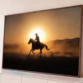 Silhueta de cowboy galopando a cavalo em contraluz ao pôr do sol com poeira dourada, quadro decorativo