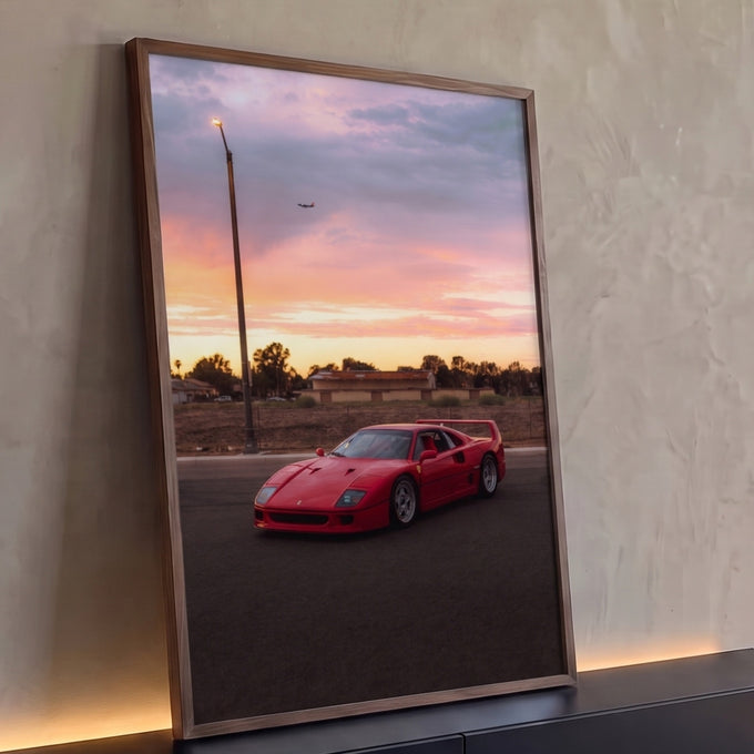 Ferrari F40 vermelha estacionada sob céu rosa do pôr do sol com avião ao fundo, quadro decorativo