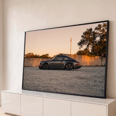 Porsche 911 clássico cinza rebaixado de perfil ao pôr do sol, sobre cascalho e muro, quadro decorativo