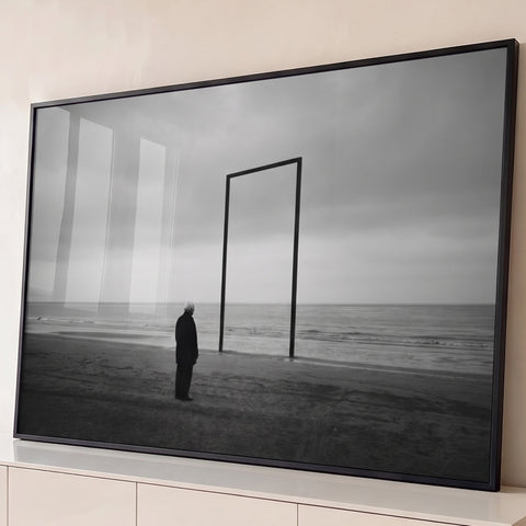 Homem idoso diante de portal metálico na praia sob céu nublado, em preto e branco, quadro decorativo