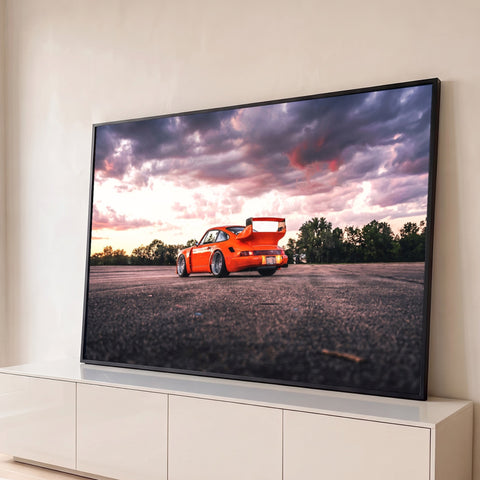 Porsche 911 laranja com aerofólio em asfalto sob céu roxo e rosa ao pôr do sol, quadro decorativo