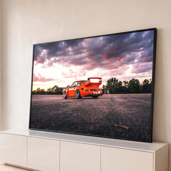 Porsche 911 laranja com aerofólio em asfalto sob céu roxo e rosa ao pôr do sol, quadro decorativo