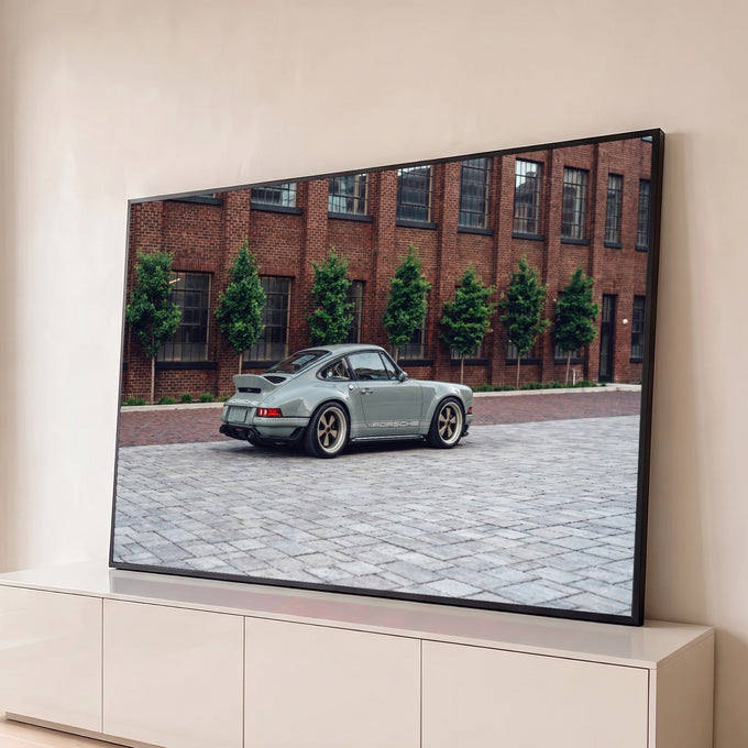 Porsche 911 clássico cinza com rodas douradas em rua de paralelepípedos e prédio de tijolos, quadro decorativo
