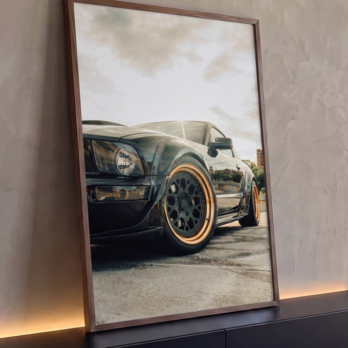 Carro esportivo preto widebody com rodas bronze em ângulo baixo sob céu claro, quadro decorativo
