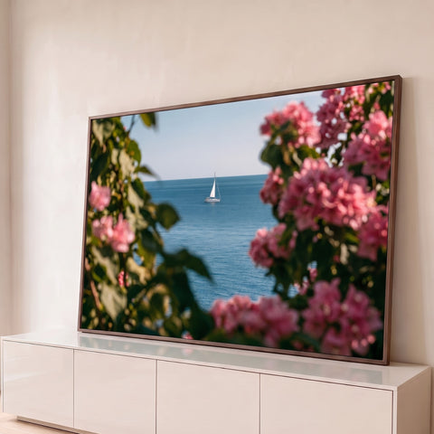 Veleiro branco no mar azul visto entre buganvílias rosa e folhagem desfocada, quadro decorativo