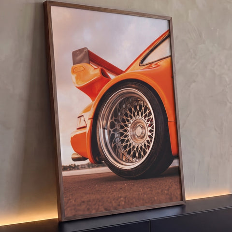Close da roda cromada de um Porsche 911 laranja com aerofólio ao pôr do sol, quadro decorativo