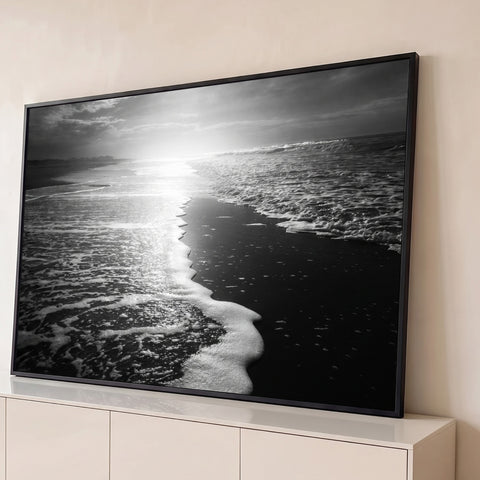 Fotografia em preto e branco de espuma do mar na areia escura com sol refletindo, quadro decorativo