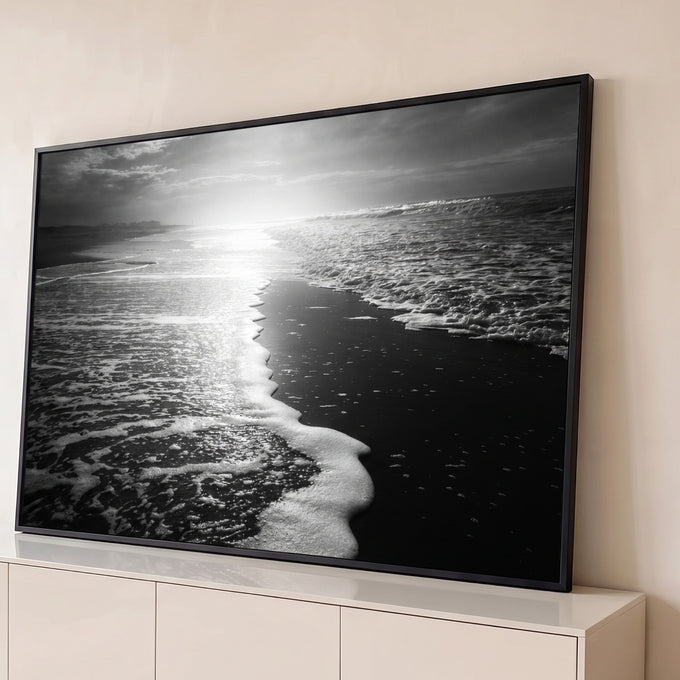 Fotografia em preto e branco de espuma do mar na areia escura com sol refletindo, quadro decorativo