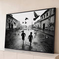 Quadro Decorativo Grande Meninos Correndo para Sala Preto | quadros decorativos para sala | dois meninos correndo com pombos voando numa rua molhada em preto e branco | Porao dos Quadros