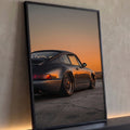 Porsche 911 cinza rebaixado com rodas douradas sob céu laranja de pôr do sol, quadro decorativo