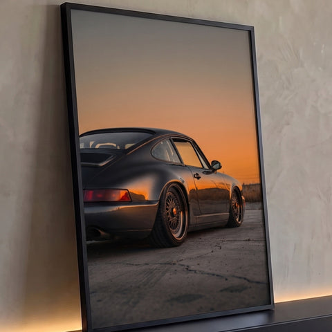 Porsche 911 cinza rebaixado com rodas douradas sob céu laranja de pôr do sol, quadro decorativo