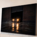 Muscle car antigo com faróis acesos saindo de galpão de tijolos à noite, reflexo no chão molhado, quadro decorativo