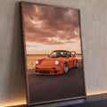 Porsche 911 laranja com aerofólio em estrada litorânea sob céu de pôr do sol, quadro decorativo