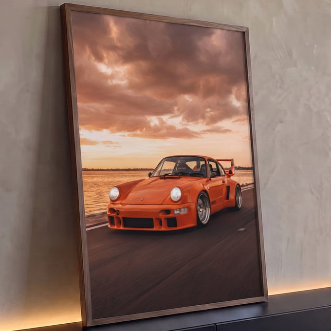 Porsche 911 laranja com aerofólio em estrada litorânea sob céu de pôr do sol, quadro decorativo