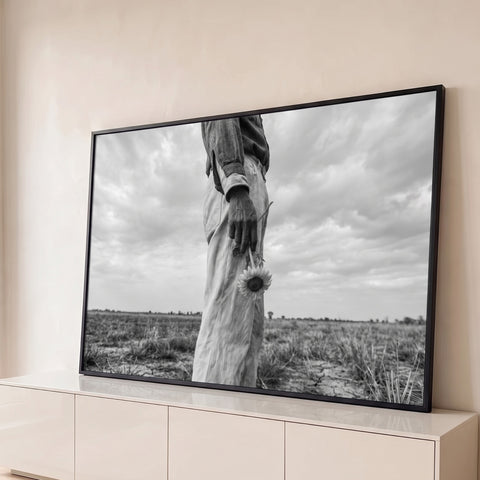 Fotografia preto e branco de lavrador segurando girassol em campo seco sob céu nublado, quadro decorativo