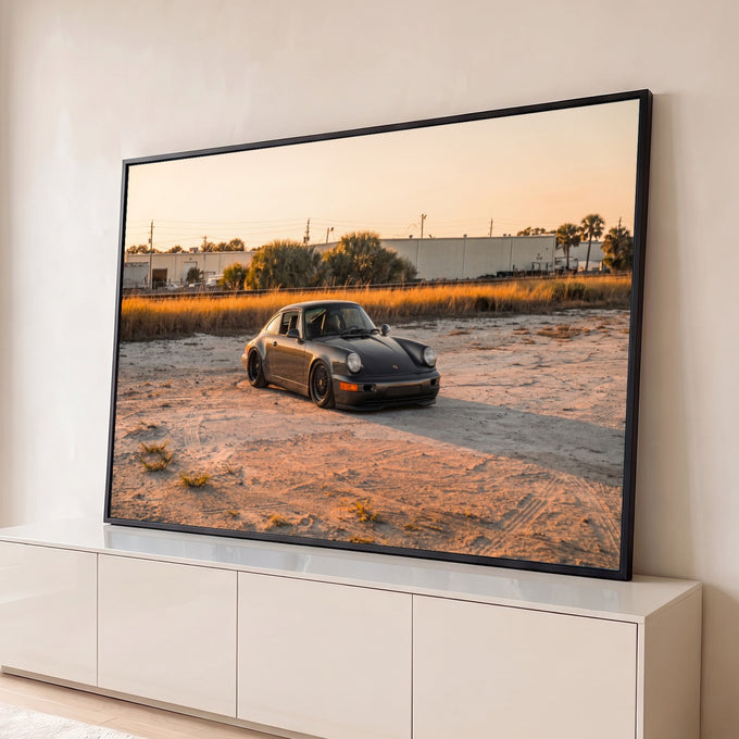 Porsche 911 clássico cinza rebaixado sobre areia com capim dourado e palmeiras ao pôr do sol, quadro decorativo
