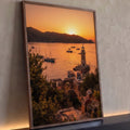 Farol de pedra e veleiros na baía ao pôr do sol laranja, com ruínas e vegetação, quadro decorativo