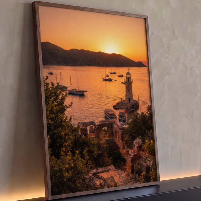 Farol de pedra e veleiros na baía ao pôr do sol laranja, com ruínas e vegetação, quadro decorativo