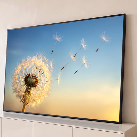 Dente de leão iluminado soltando sementes ao vento em céu azul e dourado ao entardecer, quadro decorativo