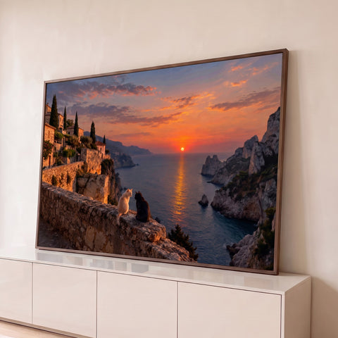 Dois gatos num muro de pedra olhando o pôr do sol laranja sobre o mar, penhascos e vilarejo, quadro decorativo