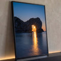 Sol se pondo através de arco de rocha no mar, reflexo dourado na água azul, quadro decorativo