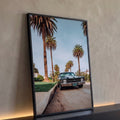 Muscle car preto com faixas brancas estacionado em rua com palmeiras e céu azul, quadro decorativo