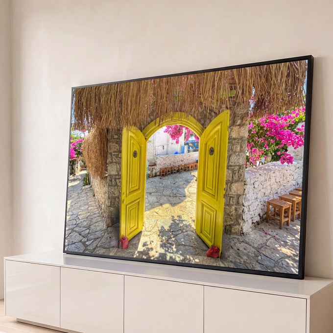 Porta amarela em arco de pedra aberta para pátio com buganvílias rosa e telhado de palha, quadro decorativo