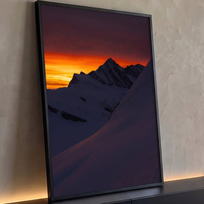 Pico nevado em silhueta contra céu laranja ao pôr do sol, encosta de neve em sombra, quadro decorativo