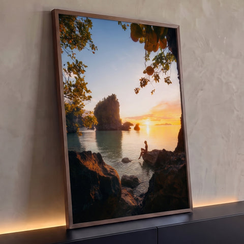Mulher sentada em rocha diante do mar ao pôr do sol entre ilhas e folhagens, quadro decorativo
