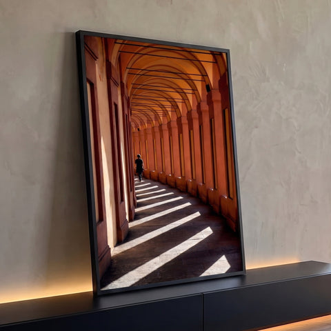 Corredor de arcos terracota com faixas de luz e sombra e pessoa caminhando ao fundo, quadro decorativo