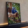 Duas araras-jacinto azuis juntinhas em galho de árvore com folhagem verde ao fundo, quadro decorativo