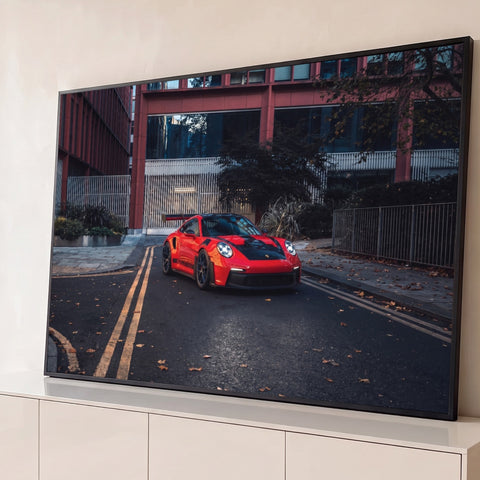 Porsche 911 GT3 RS vermelho e preto em rua urbana com folhas secas e prédio vermelho, quadro decorativo