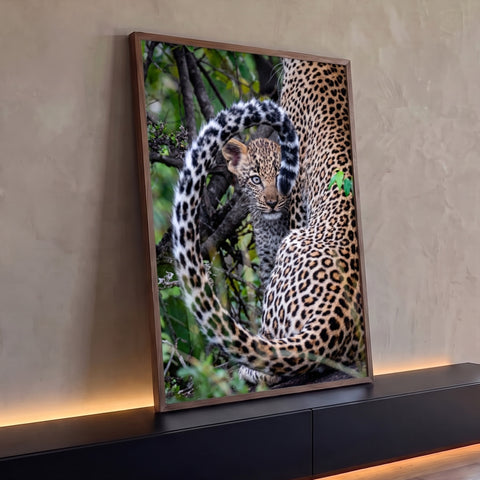 Filhote de leopardo espiando atrás da cauda da mãe entre folhagens verdes, quadro decorativo