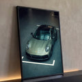 Porsche 911 verde oliva visto de cima em showroom com piso cinza e faixas brancas, quadro decorativo