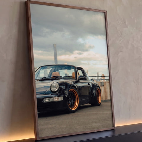Porsche 911 Targa preto com rodas bronze em terraço com arranha-céus e céu nublado, quadro decorativo
