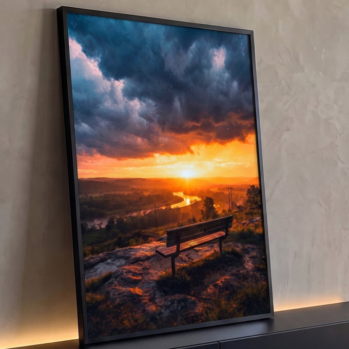 Banco de madeira em colina diante de rio sob pôr do sol laranja e nuvens escuras, quadro decorativo