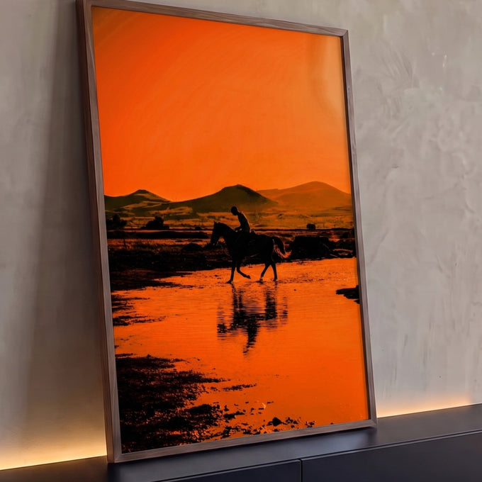 Silhueta de cavaleiro atravessando água com reflexo, montanhas e céu laranja ao pôr do sol, quadro decorativo