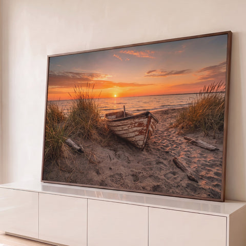 Barco de madeira rústico na areia entre capim de dunas com pôr do sol laranja no mar, quadro decorativo