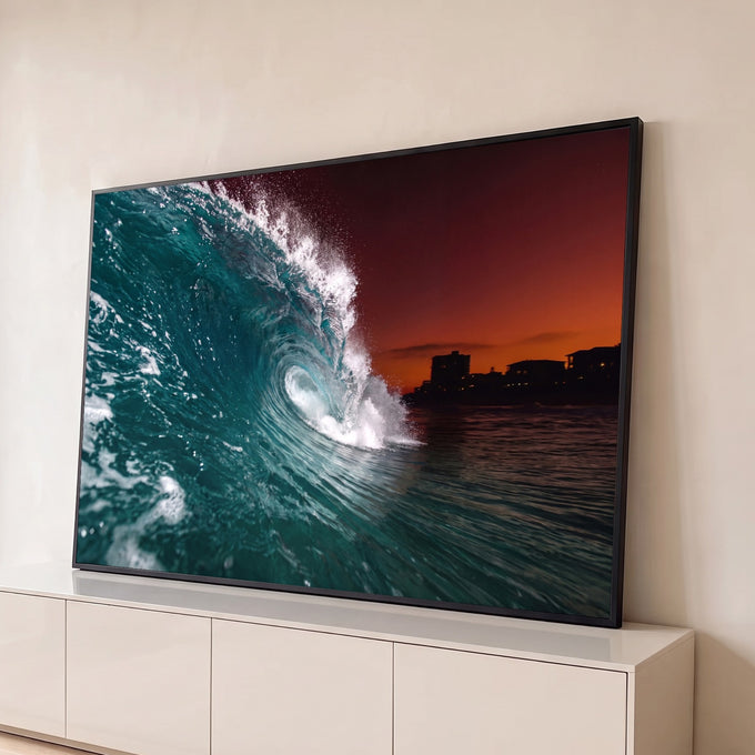 Onda do mar formando tubo azul-turquesa com céu laranja e prédios na orla ao entardecer, quadro decorativo