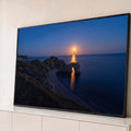 Arco de pedra no mar à noite, com falésias e lua cheia refletindo dourada na água azul, quadro decorativo