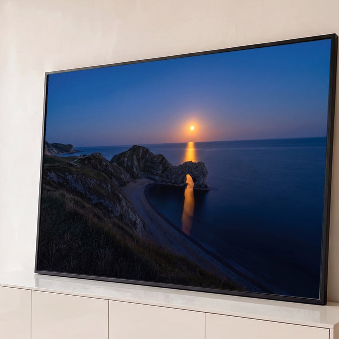 Arco de pedra no mar à noite, com falésias e lua cheia refletindo dourada na água azul, quadro decorativo