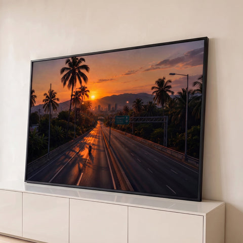 Estrada entre palmeiras com motociclista e cidade ao fundo sob pôr do sol laranja, quadro decorativo